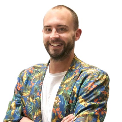 A man with a short beard and shaved head wearing a colorful floral blazer over a white shirt stands with arms crossed and smiles at the camera against a white background.