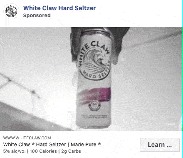A hand holds a can of White Claw Hard Seltzer outdoors. Text on the can and ad promotes the drink’s alcohol content, calories, and carbs.