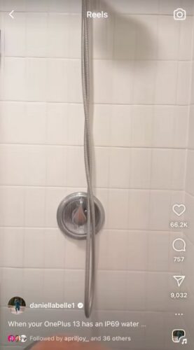 A handheld showerhead is hanging from a long hose in a tiled shower with a round faucet handle below it.