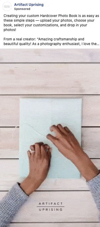 Hands flip through a custom hardcover photo book with various photos inside, placed on a light surface with "Artifact Uprising" written on the cover.