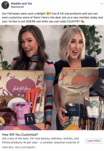 Two women stand side by side, each holding an open subscription box filled with various beauty, wellness, and lifestyle products.