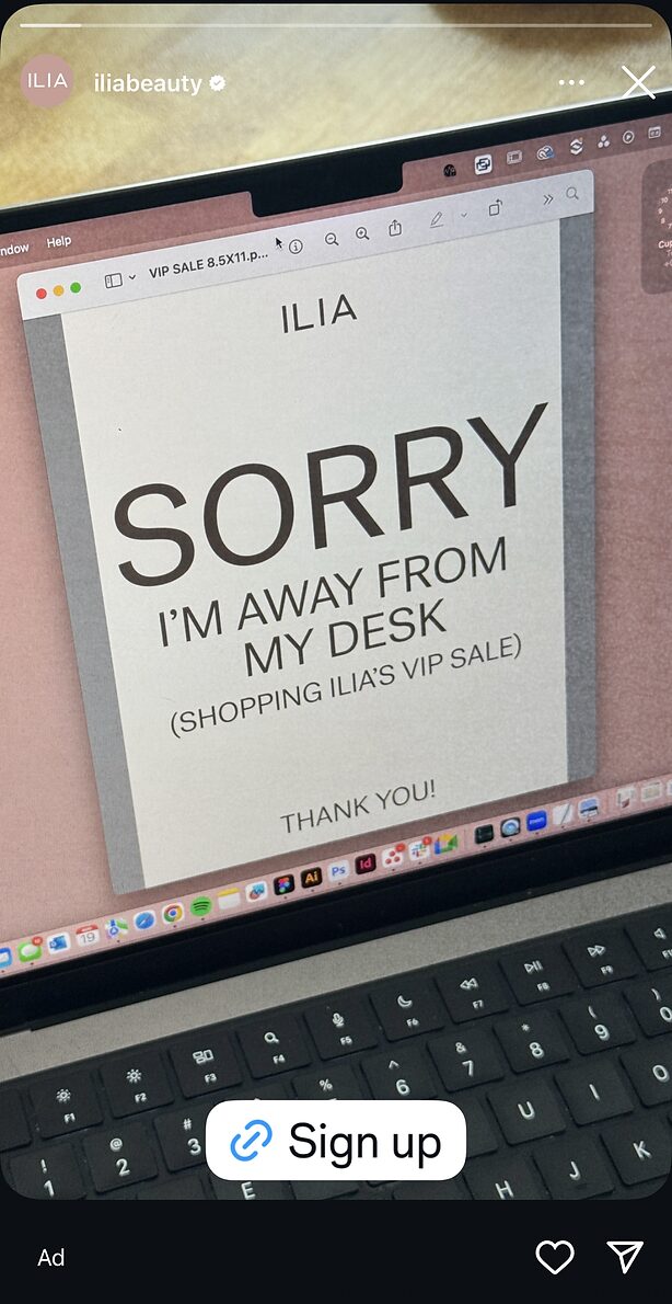 A laptop screen displays a sign that reads "SORRY I'M AWAY FROM MY DESK (SHOPPING ILIA'S VIP SALE)" with a keyboard visible at the bottom.