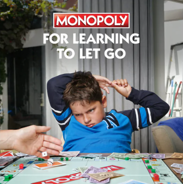 A boy in a blue shirt looks frustrated while playing Monopoly, with a hand rolling dice and game pieces scattered on the table. Text above reads "MONOPOLY FOR LEARNING TO LET GO.