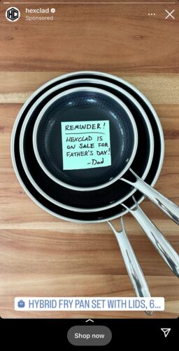 Three stainless steel frying pans stacked on a wooden surface with a sticky note on the top pan reminding that HexClad is on sale for Father’s Day.