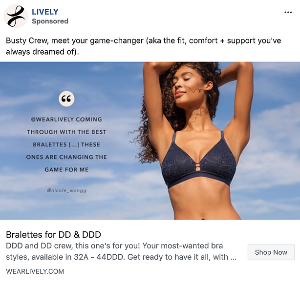 A woman outdoors wearing a navy blue bralette with thin straps, raising her arms above her head and smiling against a clear blue sky.