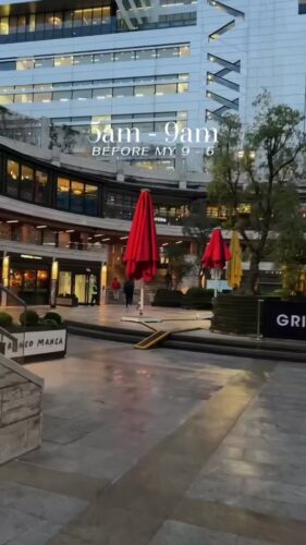 A modern outdoor plaza with closed red and yellow umbrellas, empty seating areas, and office buildings in the background. Text overlay reads "5am - 9am BEFORE MY 9 - 5".