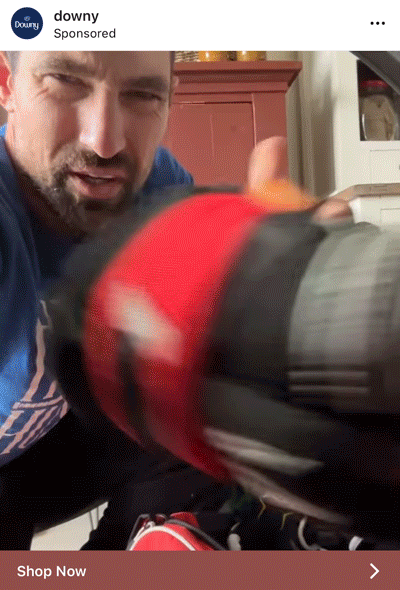 A man in a blue shirt holds a red and black athletic shoe close to the camera, partially obscuring his face.