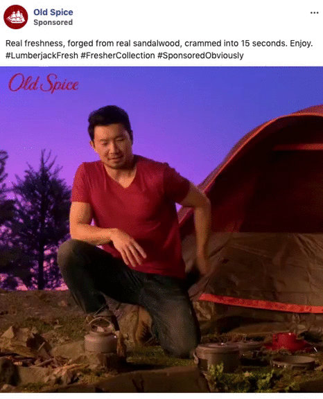 A man in a red t-shirt kneels by a campfire site near a tent at sunset, with Old Spice branding and text above him.