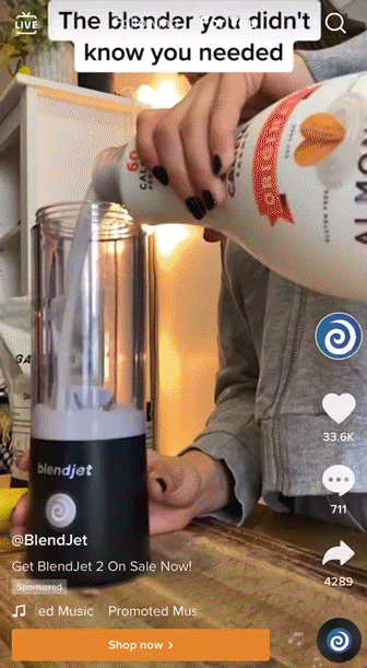 A person pours liquid from a large bottle into a BlendJet blender on a wooden table, with text overlay reading, "The blender you didn't know you needed.