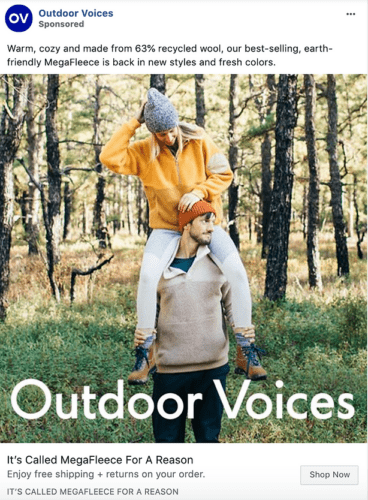 A woman in a yellow fleece sits on a man's shoulders outdoors; both wear beanies and fleece tops in a grassy area. Text promotes Outdoor Voices' recycled wool MegaFleece clothing.