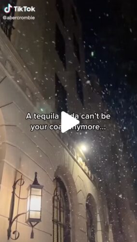 Snow falls at night outside a building with arched windows and a lantern; overlaid text reads, "A tequila soda can't be your coat anymore...