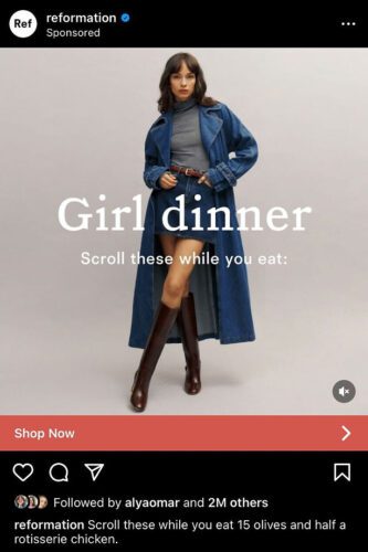 A woman wearing a long blue coat, gray top, skirt, and knee-high brown boots stands against a plain background. Text reads: "Girl dinner. Scroll these while you eat.