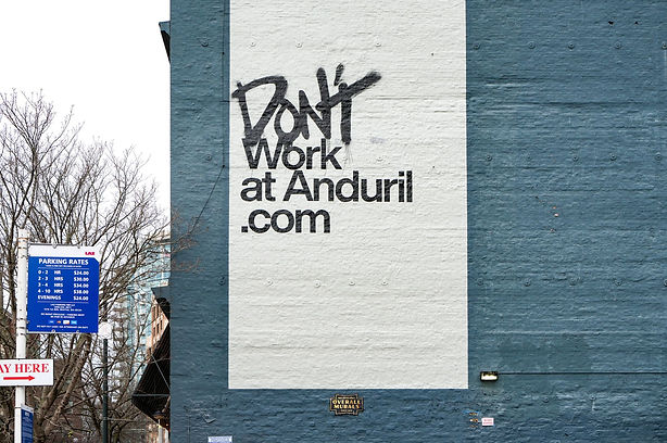 A large white mural on a blue wall displays the text: "DON’T Work at Anduril.com" in bold, black letters.