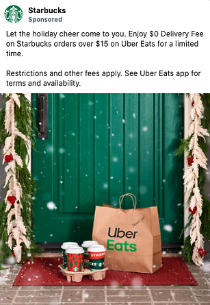 A Starbucks Uber Eats paper bag and three holiday-themed coffee cups sit on a doorstep decorated with greenery and snow.