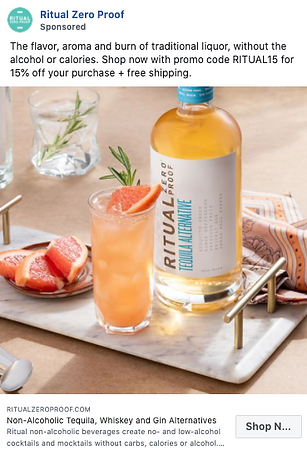 A bottle of Ritual Zero Proof Tequila Alternative stands beside a glass of grapefruit cocktail with a wedge garnish; both are on a table with sliced grapefruit and bar tools.
