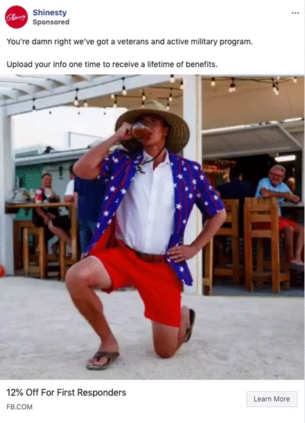 A man in a star-spangled shirt, red shorts, and a straw hat kneels and drinks from a glass at an outdoor social event; people watch in the background.