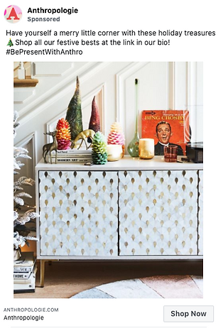 A sideboard decorated with colorful bottle brush trees, candles, books, a gold ornament, and framed art, set against a staircase for a festive holiday display.