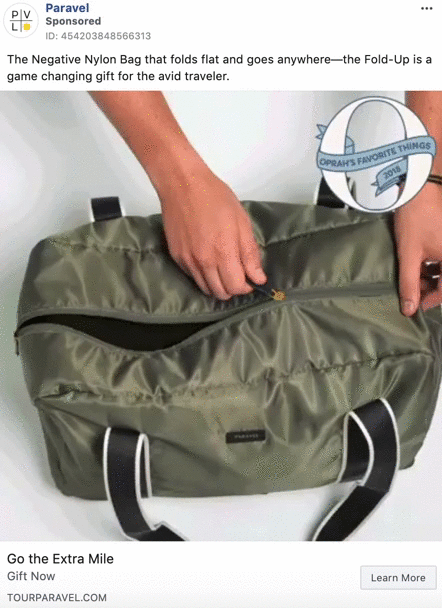 A person opens the zipper of a green nylon travel bag with black and white handles. The bag displays an "Oprah's Favorite Things 2018" badge.