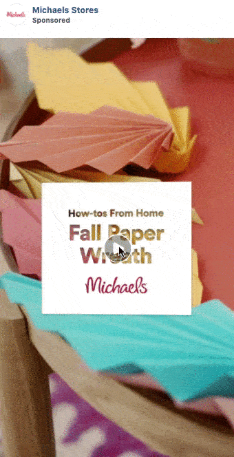 Colorful folded paper leaves decorate a round surface. Text overlay reads: "How-tos From Home: Fall Paper Wreath, Michaels." Play button in the center.