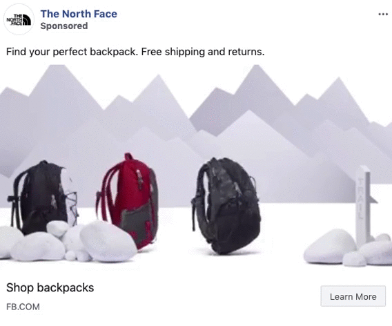 Three backpacks in different colors are displayed on a white surface with white rocks and stylized gray mountain shapes in the background.