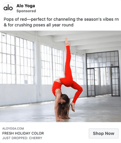 Woman in a spacious, sunlit studio wearing bright red yoga attire performs a handstand with one leg bent and the other extended upward.