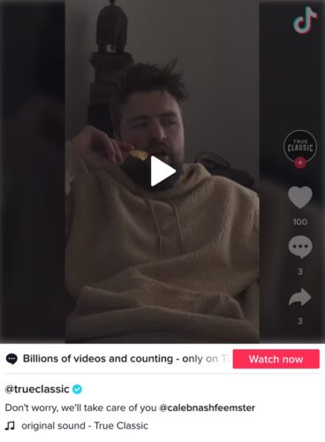 A man in a beige hoodie sits indoors eating a snack, with TikTok interface elements visible on the right side of the screen.