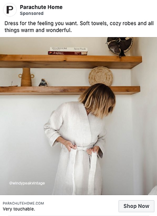 A person wearing a light-colored robe stands in a room with wooden shelves decorated with books and baskets.
