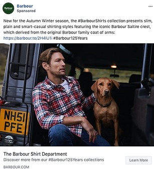 A man in a red plaid shirt sits in the open back of a vehicle beside a brown dog, with a countryside background visible.