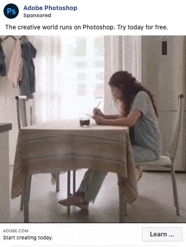 A woman sits at a kitchen table drawing on paper with a pencil, sunlight streaming through a window behind her.