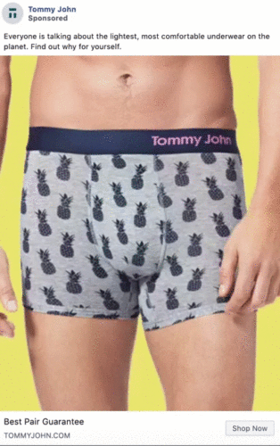 A man wearing gray Tommy John boxer briefs with a black pineapple pattern, standing in front of a yellow background.