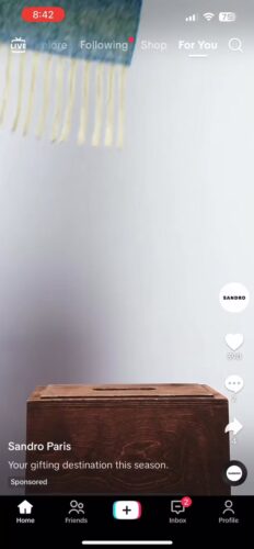 A brown wooden box sits against a plain light wall, partially covered by a hanging textile with fringes. TikTok interface elements are visible on the screen.