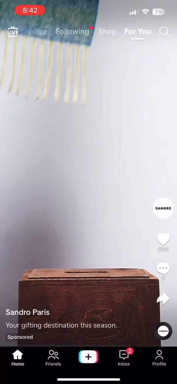 A brown wooden box sits against a plain light wall, partially covered by a hanging textile with fringes. TikTok interface elements are visible on the screen.