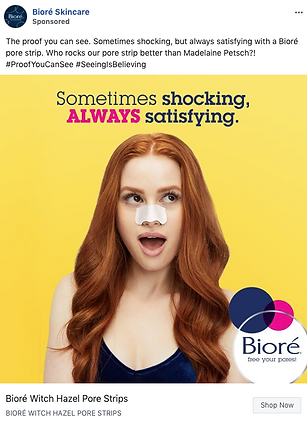 A woman with long red hair wears a Biore pore strip on her nose against a yellow background, with text that reads, "Sometimes shocking, ALWAYS satisfying.