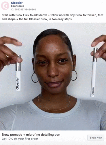 A person holds up two Glossier brow products, one in each hand, in front of their face. The image promotes brow pomade and a microfine detailing pen.