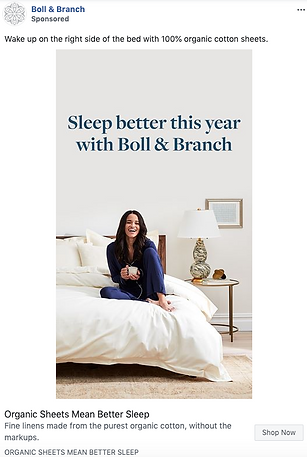 A woman sits smiling on a neatly made bed with white sheets in a bright, modern bedroom. Text reads, "Sleep better this year with Boll & Branch.
