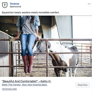 A person in jeans, a denim shirt, and brown boots sits on a fence in a barn next to a white and brown horse.