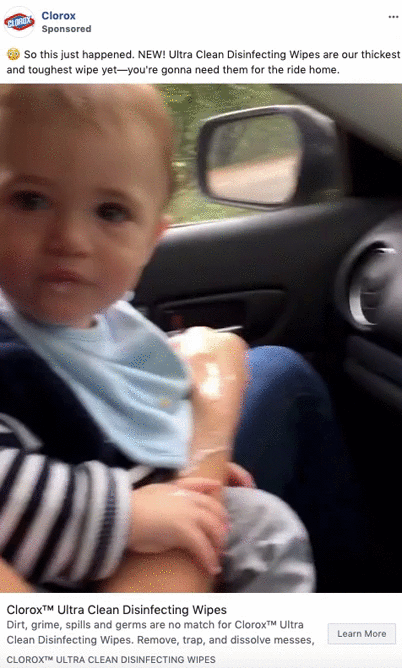 A young child sits in a car seat beside an adult, with the adult's hand visible holding an object. The interior of the car is visible in the background.