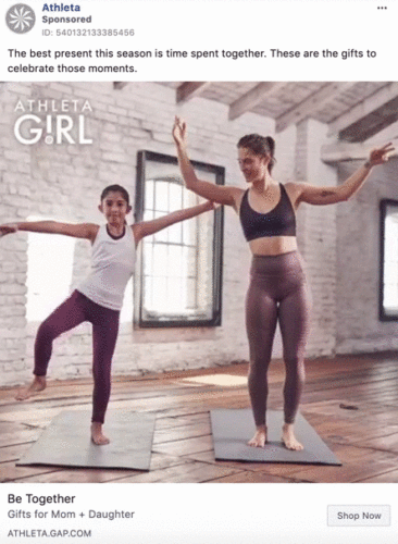 An adult woman and a young girl practice yoga together on mats in a bright room with brick walls and large windows.