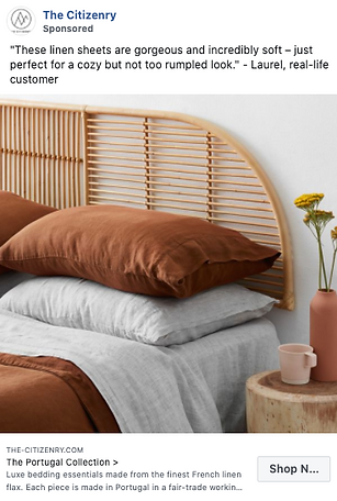 A neatly made bed with brown linen sheets, light gray pillowcases, a rattan headboard, and a small side table with a pink vase and flower.