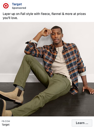 A man sits on the floor wearing a plaid flannel shirt over a beige top, olive green pants, and tan boots.