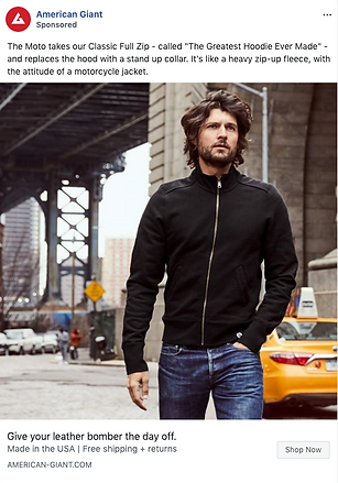 A man wearing a black zip-up jacket and blue jeans stands outdoors under an urban bridge, looking slightly to the side with one hand in his pocket.