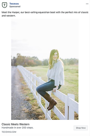 A woman in a gray sweater and jeans sits on a white fence in a rural setting, wearing brown knee-high equestrian boots.