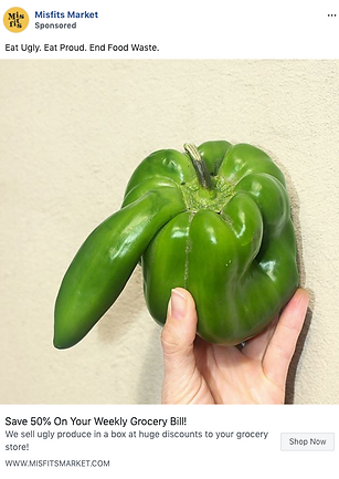 A hand holding a large, irregularly shaped green bell pepper with a prominent protrusion, against a plain beige background.