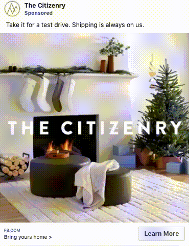 A living room with a lit fireplace, stockings on the mantel, a small decorated Christmas tree, two green ottomans, and neatly stacked firewood.