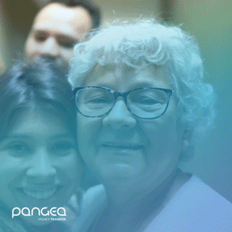 An older woman with white hair and glasses smiles with a younger woman in front of her. A man stands behind them. The image has a blue overlay and a "pangea money transfer" logo.