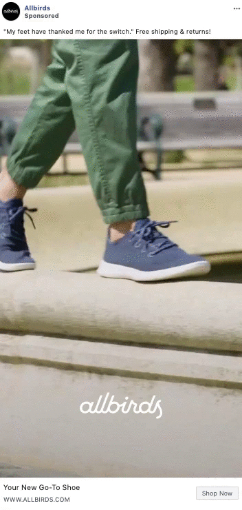 Person wearing green pants and blue Allbirds sneakers walks along a low concrete wall in an outdoor park setting.