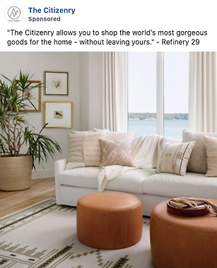 A modern living room with a white sofa, neutral pillows, two brown ottomans, a plant, framed art on the wall, and large windows overlooking water.