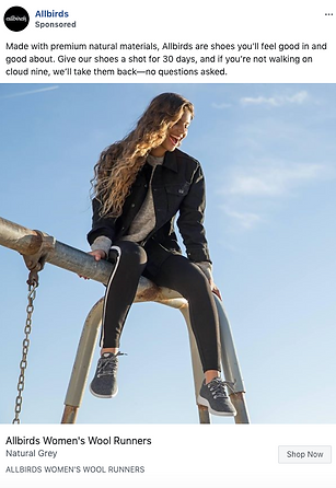 A woman sits on top of a metal climbing frame outdoors, wearing a black jacket, black pants, and grey Allbirds Wool Runners, with clear blue sky in the background.