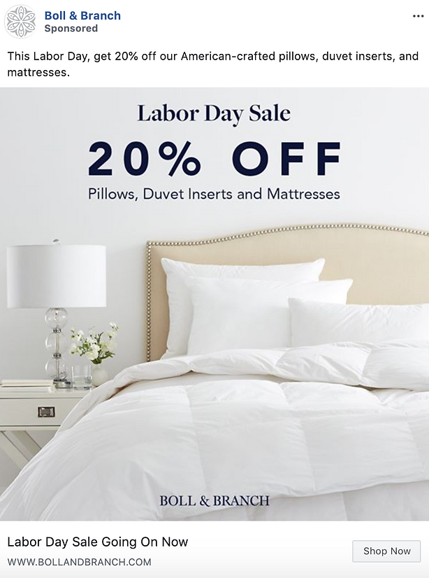 A neatly made bed with white bedding and pillows, a nightstand with a lamp, and text announcing a 20% off Labor Day sale on pillows, duvet inserts, and mattresses.