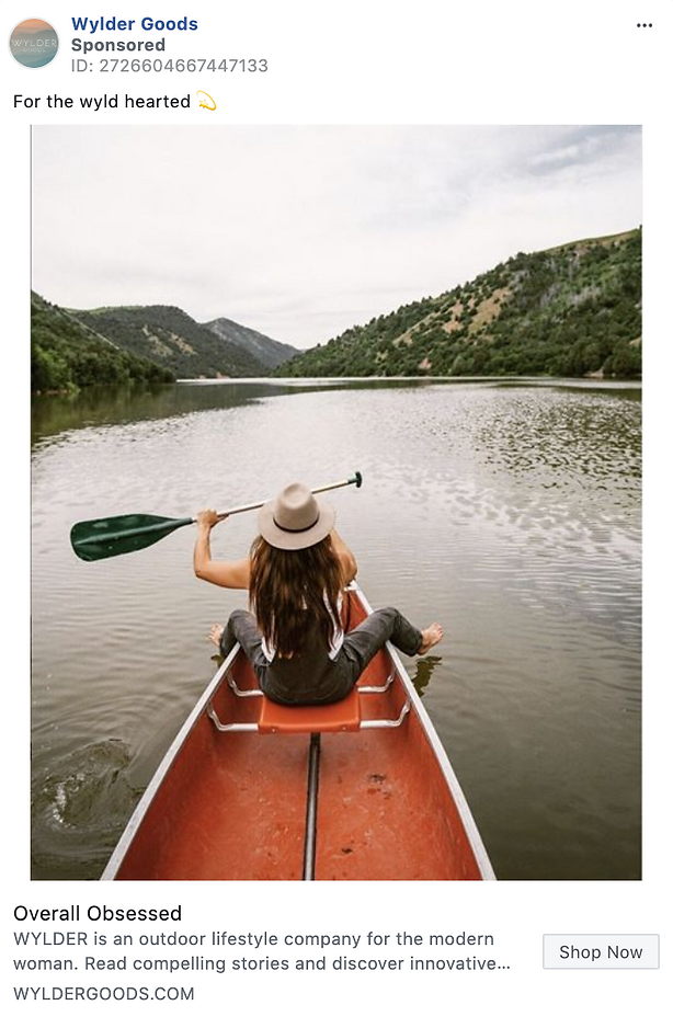 A person in a hat paddles a red canoe on a calm river surrounded by green hills under a cloudy sky.